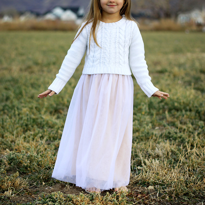 A little girl standing in a field wearing a long skirt