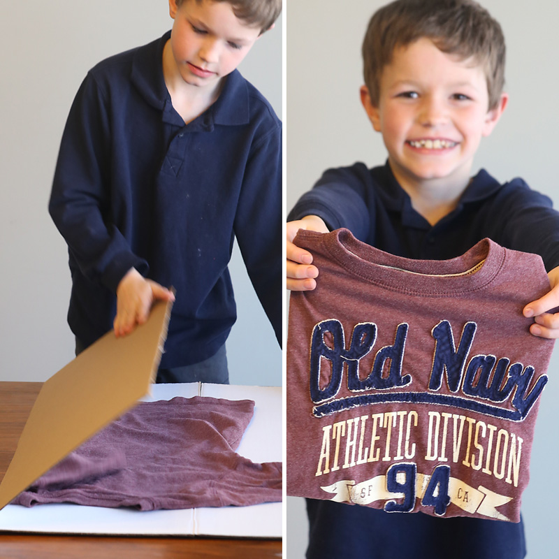 A boy using a large piece of cardboard to neatly fold a t-shirt