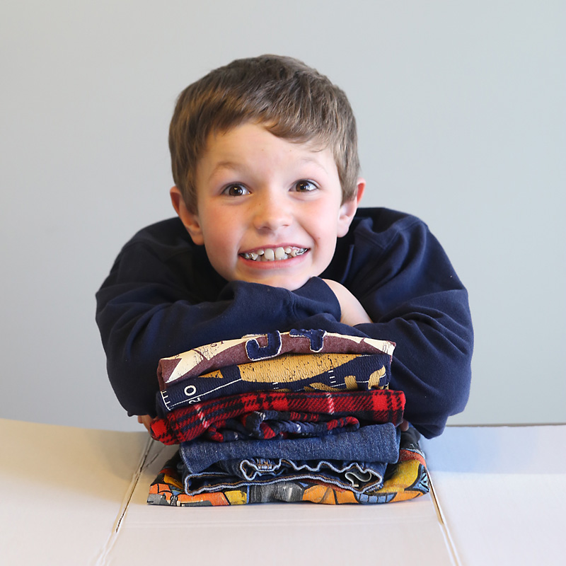 A little boy is leaning on a stack of folded laundry