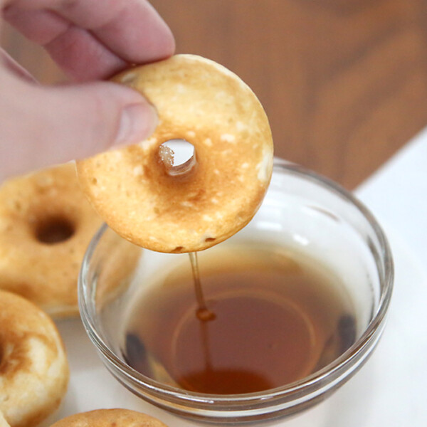 Hand dipping a pancake donut into syrup