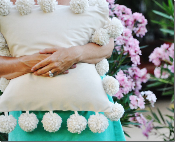 Person holding a pillow with large pom poms around the edges
