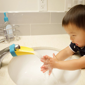 A baby washing his hands at a sink that\'s using a faucet extender