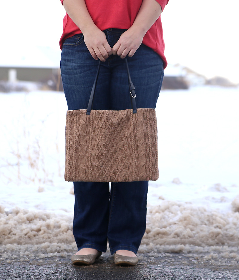 A person standing in the snow holding a laptop tote made from a sweater