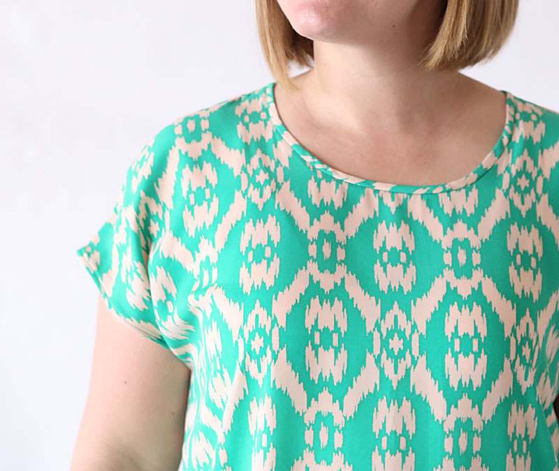 A closeup of the neckline and sleeve of a green tunic top