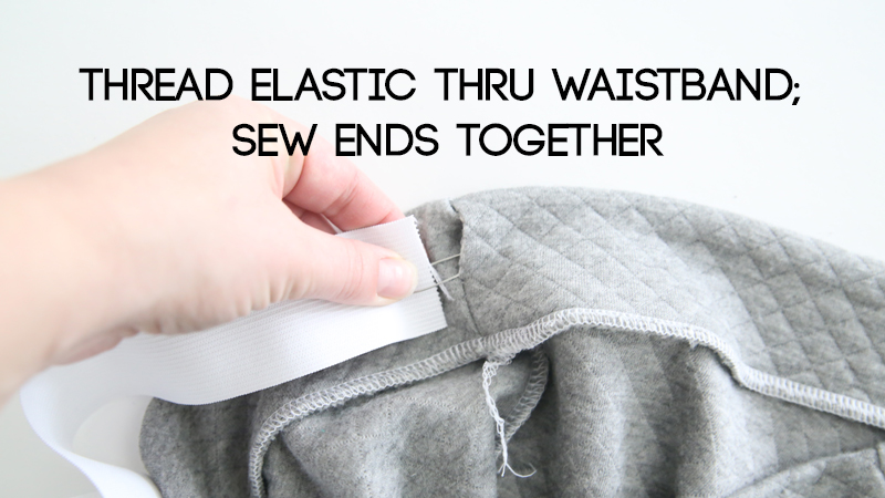 Hand using safety pin to thread elastic through waistband