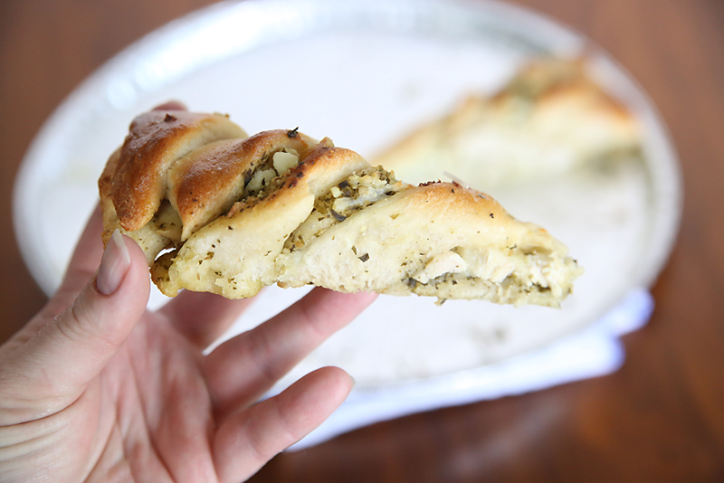 A hand holding a slice of pesto chicken tear and share