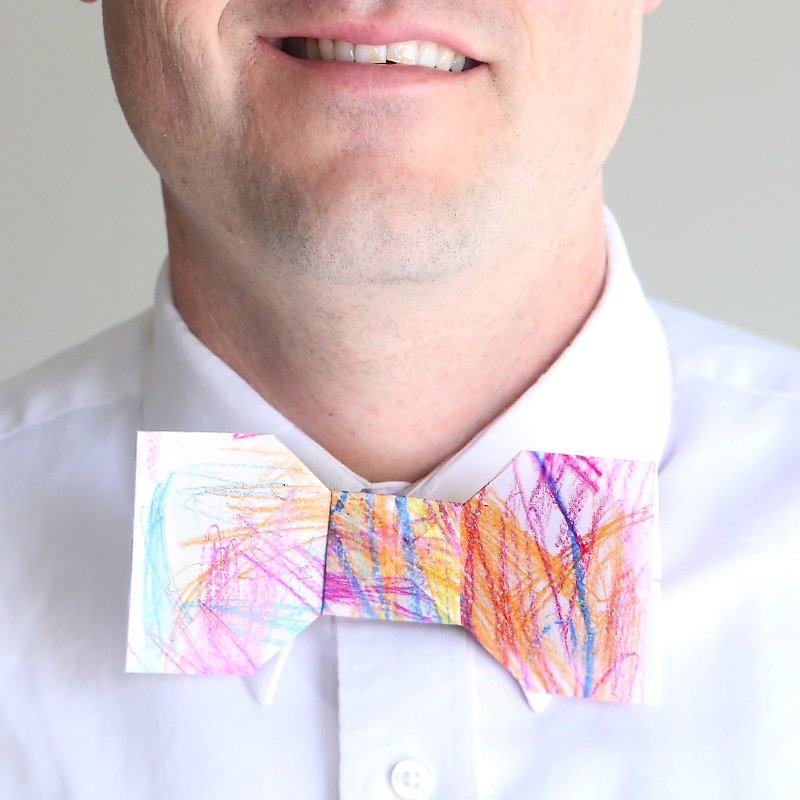 A man wearing a paper orgami bowtie that\'s been colored