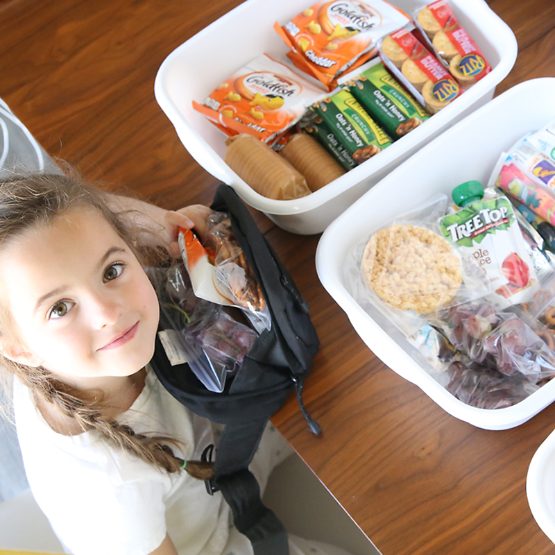 A little girl looking at bins full of health snacks, filling a fanny pack