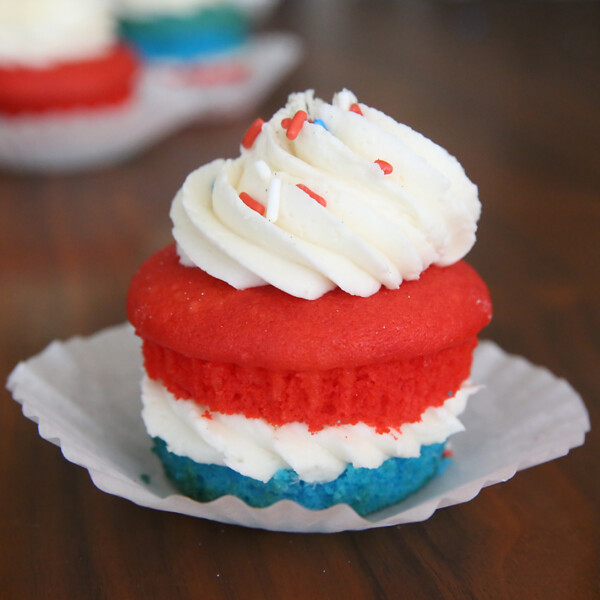 Cupcake made with layers of blue cake, white frosting, red cake, more white frosting, sprinkles