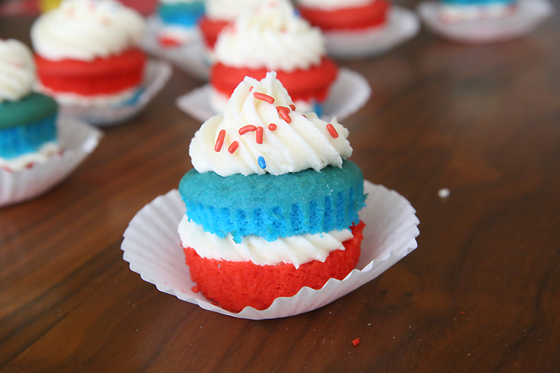 Cupcake with layers of red and blue cake with white frosting and sprinkles