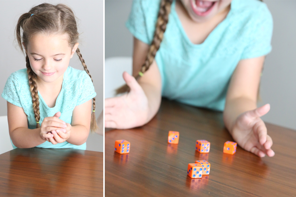 A little girl sitting at a table rolling dice and having fun