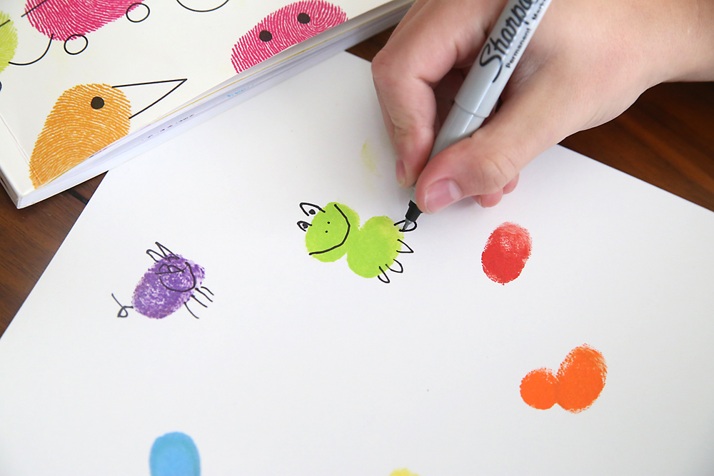 Boy drawing on two green fingerprints to make it look like a frog