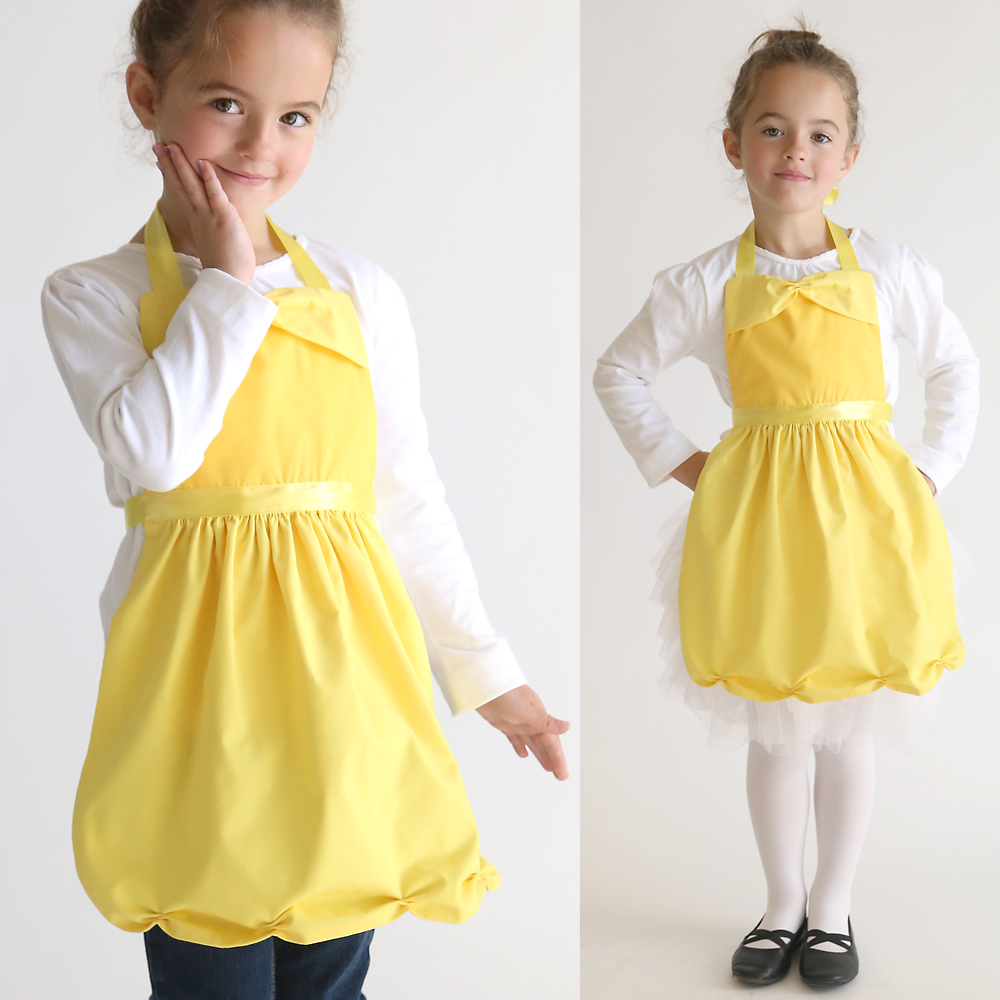 A little girl wearing a yellow apron that looks like Belle\'s dress from beauty and the beast