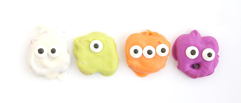 Pretzels dipped in white, green, orange, and purple candy melts with candy eyes to look like ghosts and monsters