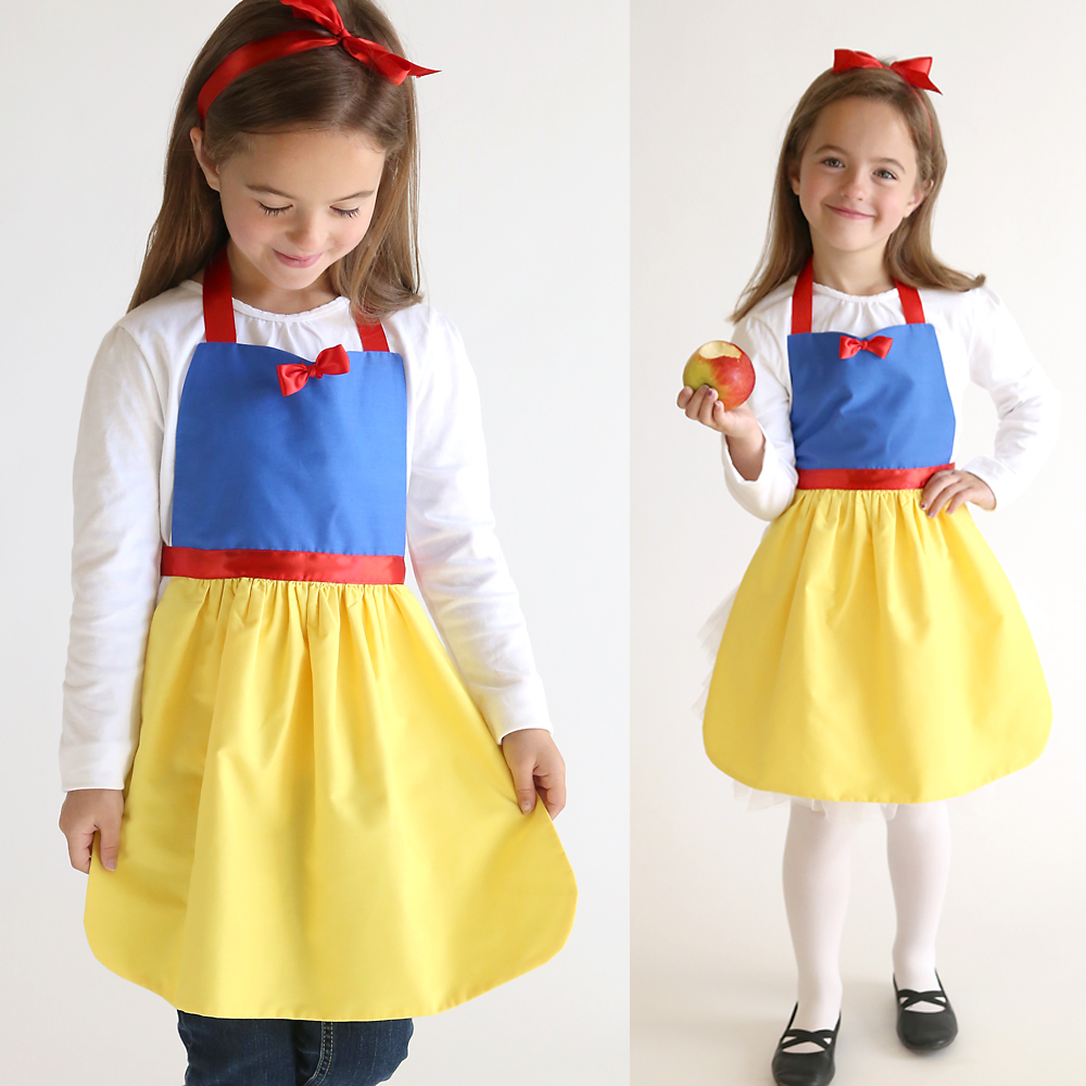 A young girl wearing a Snow White princess dress up apron, holding an apple