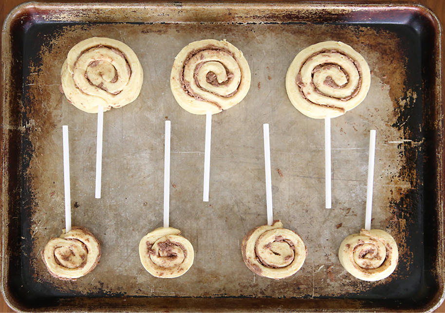 Rolled up cinnamon rolls on a baking sheet with candy sticks stuck into them
