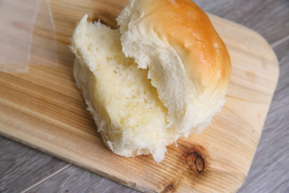 homemade dinner roll on a wood cutting board, torn in half with melted butter on it