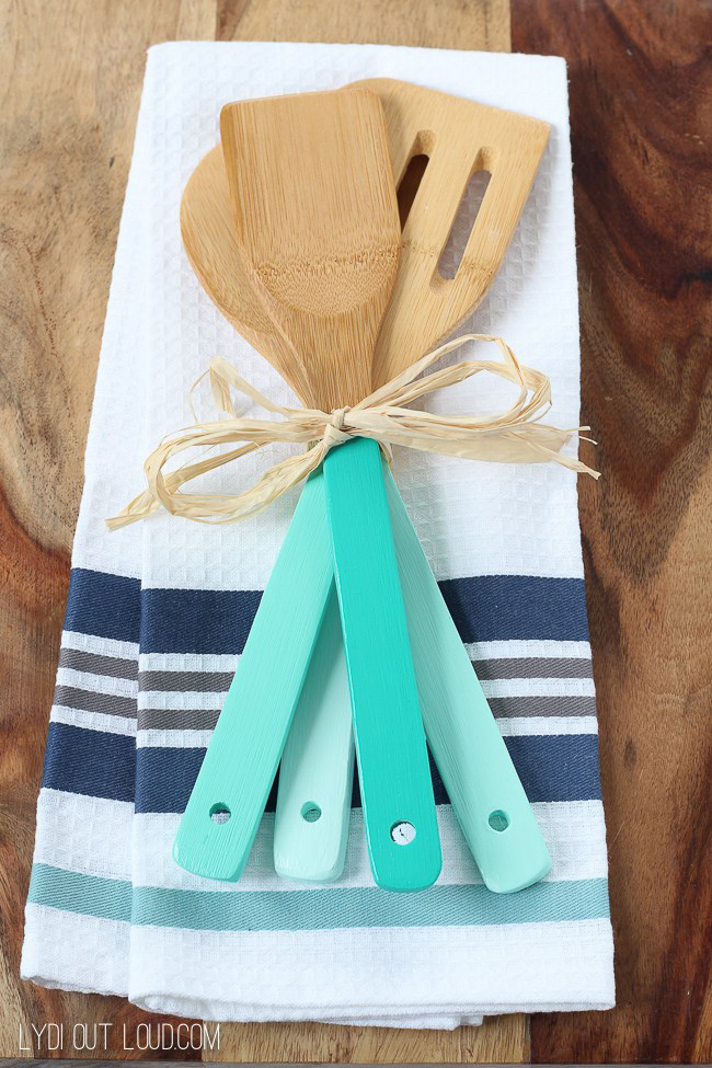 Wood spoons with pretty teal paint dipped handles tied with a bow, on a tea towel