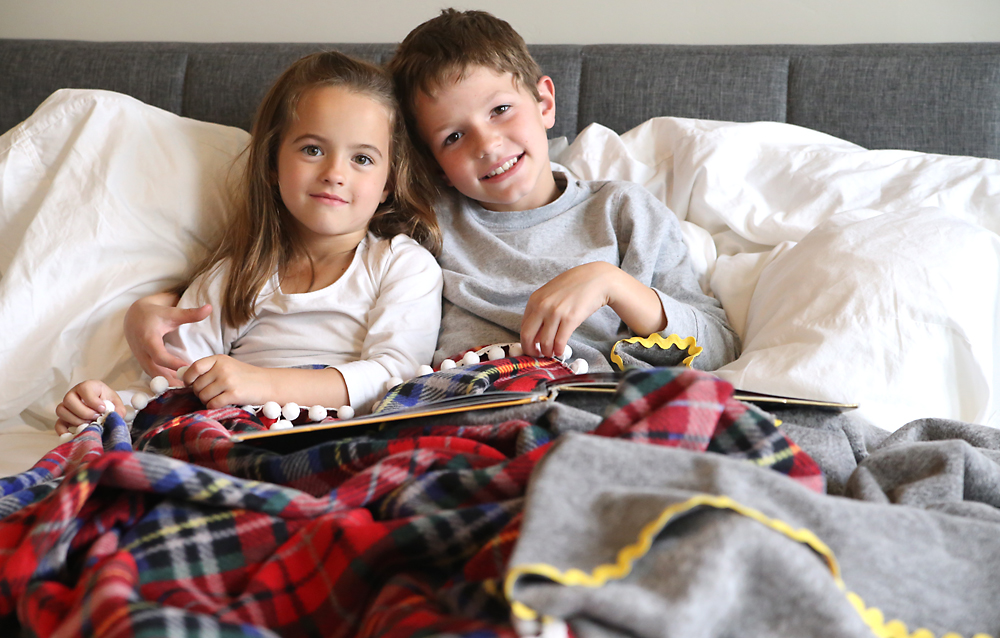 A little girl sitting on a bed with a fleece blanket