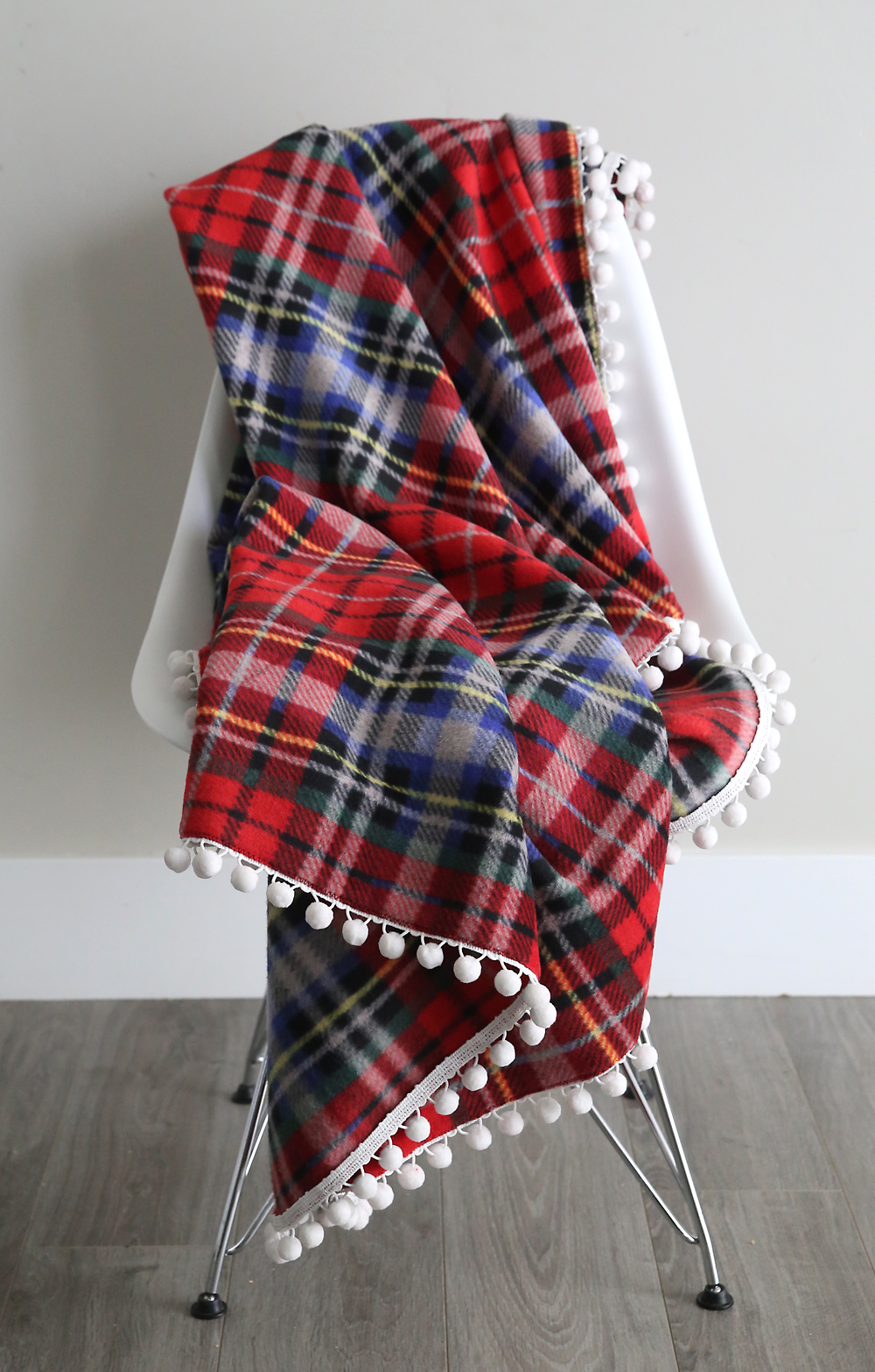 DIY fleece blanket trimmed with pom poms draped over a chair