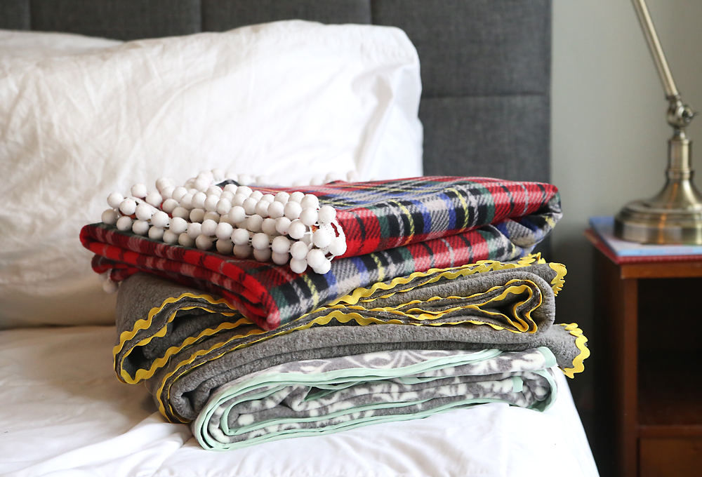 Three DIY fleece blankets folded on a bed