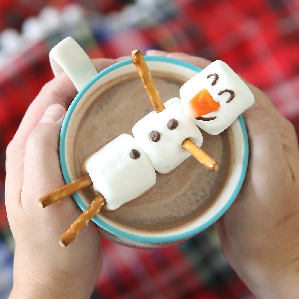 hands holding mug of hot cocoa with marshmallow snowman floating in it