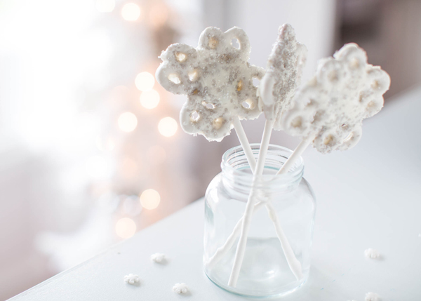 White chocolate covered pretzels that look like snowflakes on candy sticks in a jar