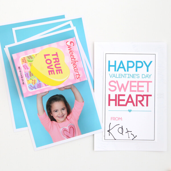 Photo of a little girl with her arms above her head with a box of Sweethearts candy attached so it looks like she's holding the box; sweetheart Valentine's card