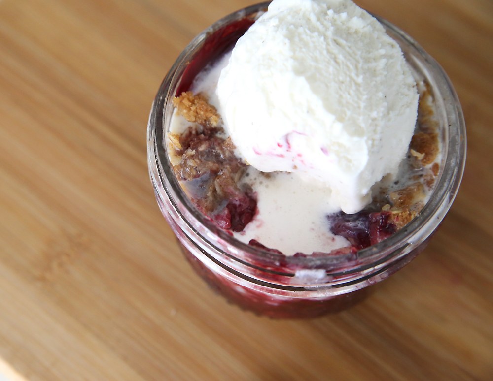 Single serving berry crisp in a mason jar with scoop of vanilla ice cream