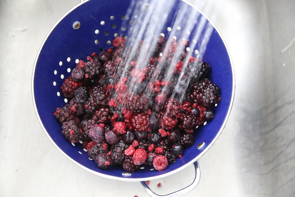 frozen berries in a colander being rinsed with water