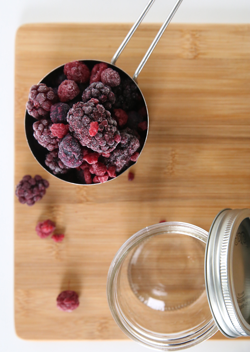 frozen berries in a measuring cup on a wood cutting board with mason jar