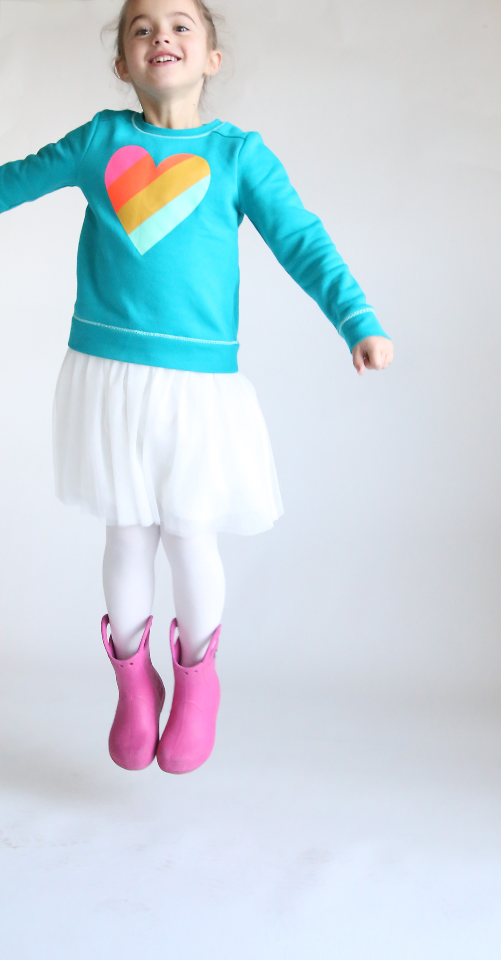 A little girl wearing a sweatshirt dress and jumping