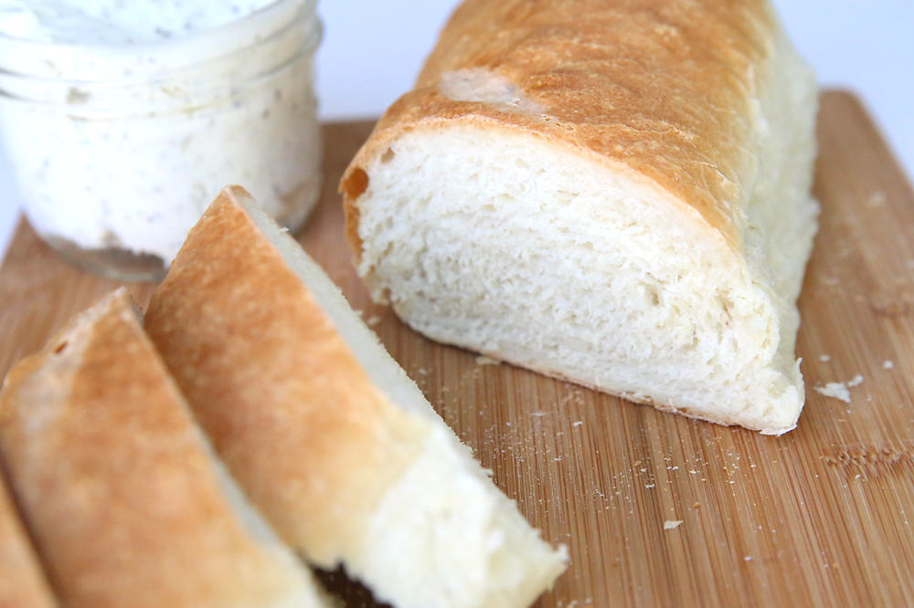 A loaf of homemade french bread cut in slices on a wood cutting board