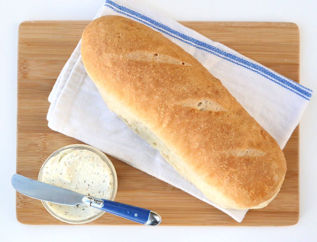 A loaf of homemade french bread on a kitchen towel on a cutting board, with garlic butter