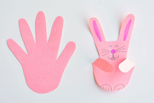handprint shape cut from pink paper, then folded and decorated to look like a bunny