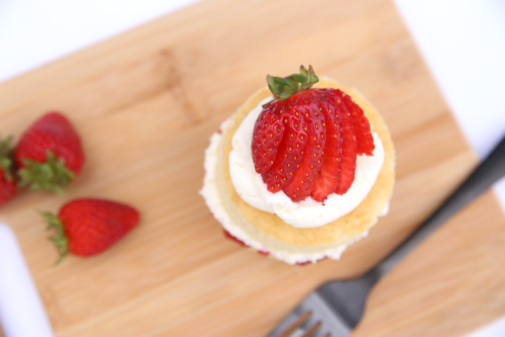 A piece of strawberry shortcake on a wood cutting board with a fork