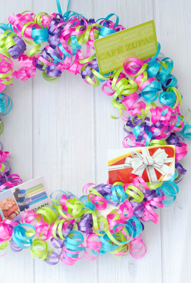 A wreath covered in colorful ribbon with multiple gift cards attached for teacher