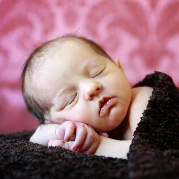 A newborn baby lying down on his arms covered with a blanket