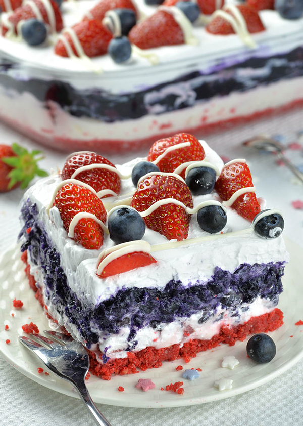Red and blue layered cake with cream and topped with berries for Fourth of July