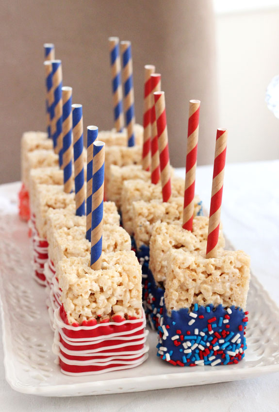 Rice krispie treats dipped in red and blue candy coating with straws