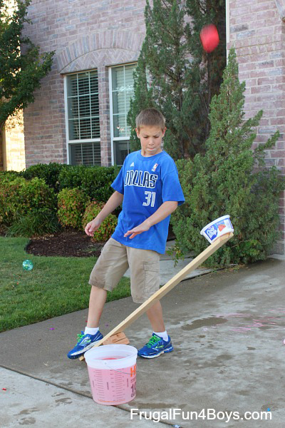 A boy stomping on one end of a board that launches a water balloon 