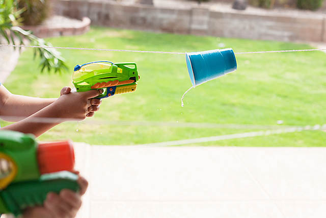 A child shooting a water gun into a cup that\'s suspended on a string