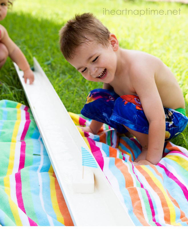 A small child sitting on a beach towel watching small boats in a rain gutter