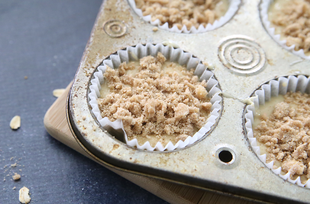 A close up of a muffin tin filled with oatmeal batter and topped with struesel