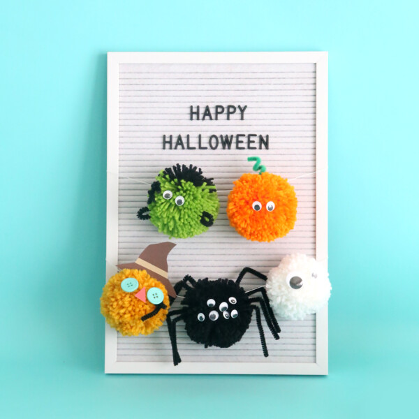 Halloween pom pom characters hanging on a sign that says Happy Halloween