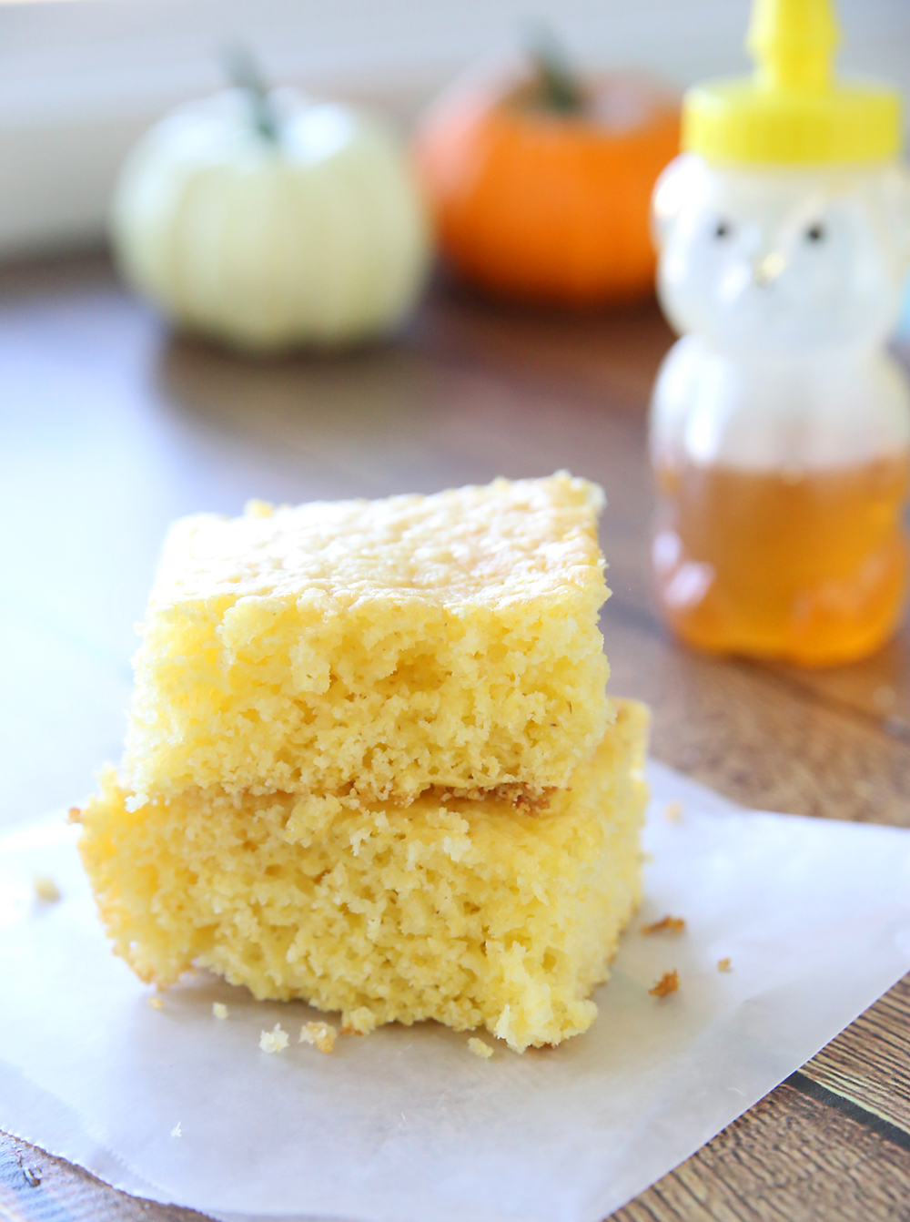 Two pieces of cornbread stacked on a table, honey in the background