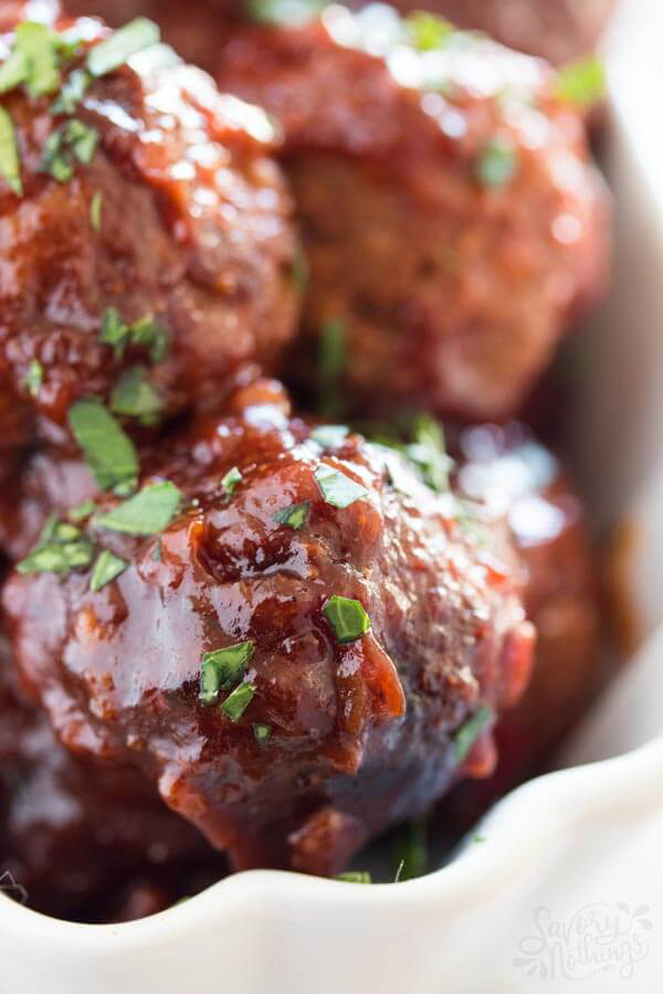 A close up of make ahead sticky meatballs sprinkled with herbs for Thanksgiving