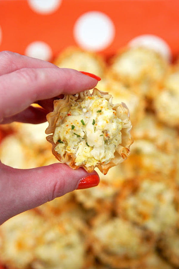 Hand holding an artichoke parmesan bite, make ahead Thanksgiving side dish