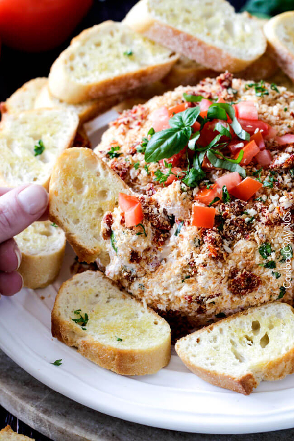 Bruschetta cheeseball topped with chopped tomatoes, surrounded by slices of baguette