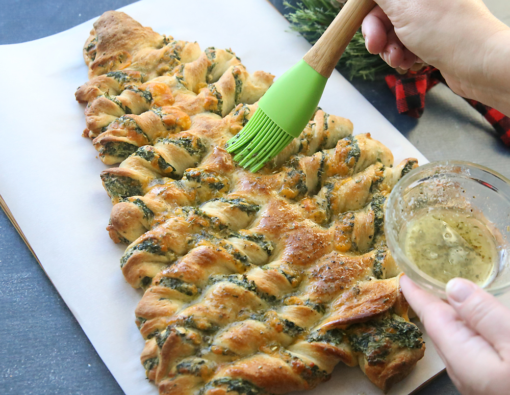 Hand brushing melted butter on baked Christmas tree breadsticks